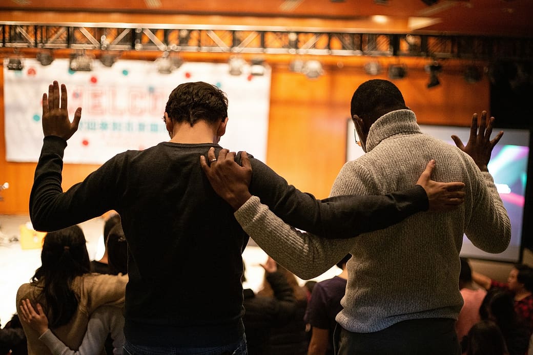 Two men praying side by side with hands raised at a church gathering